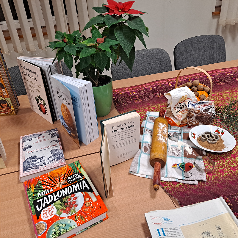 Dekoracja stołu: kolorowy obrus, książki o tematyce kulinarnej, wałek obsypany mąką, kwiat - gwiazda betlejemska