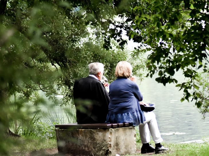 kobieta i mężczyzna w dojrzałym wieku, siedzą tyłem  na ławce nad jeziorem