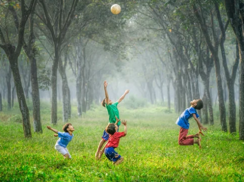 Czwórka dzieci gra w piłkę, w tle trawiasta droga w lesie