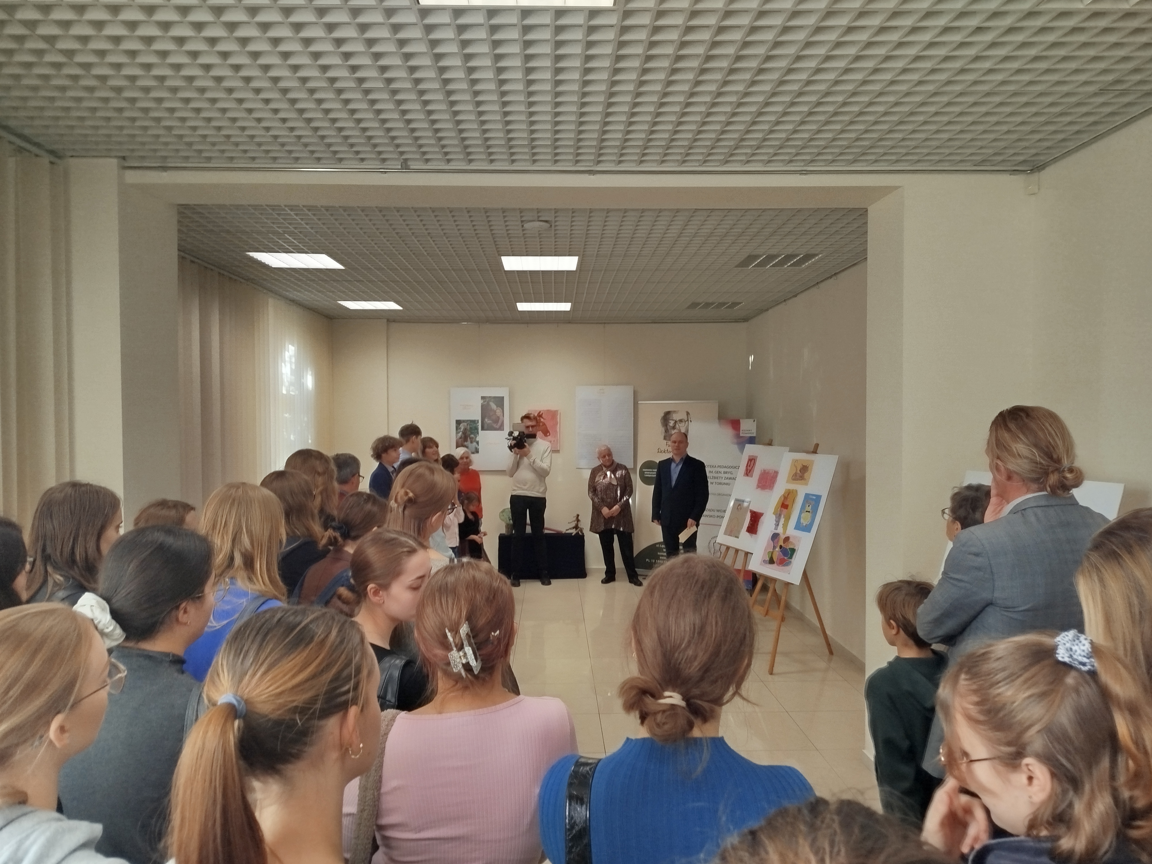 Grupa ludzi stoi w sali wystawowej Biblioteki Pedagogicznej w Toruniu.